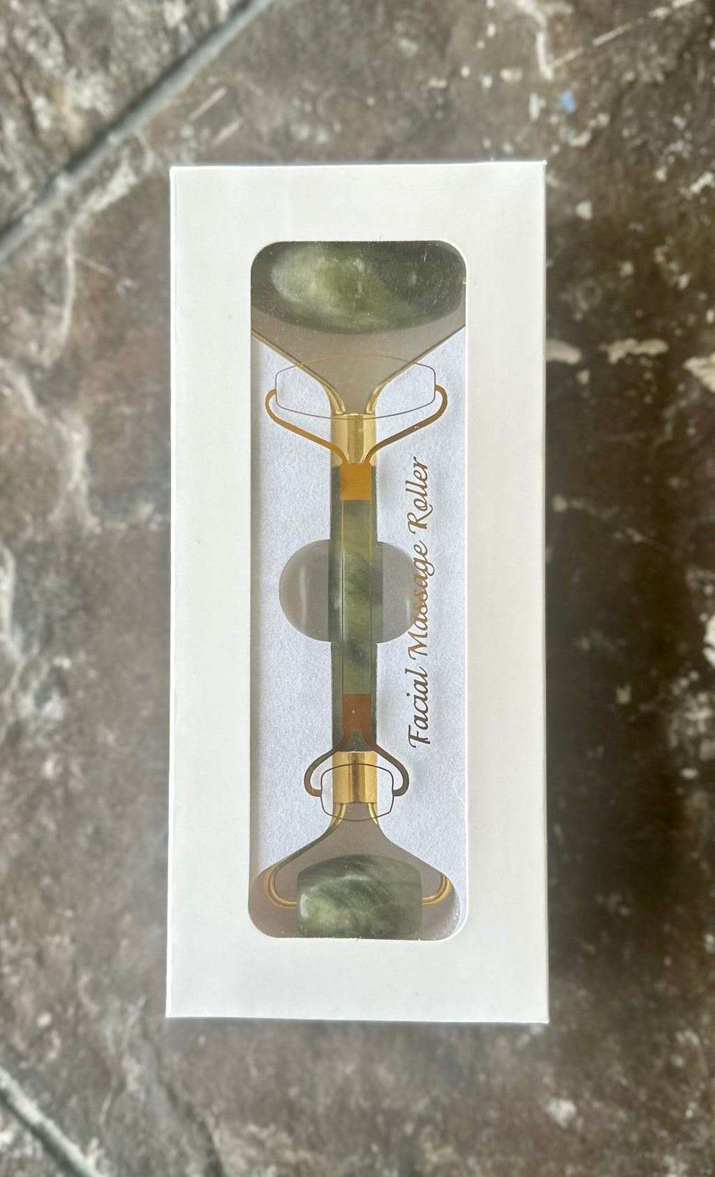 Green double-ended jade facial roller in a white windowed box.