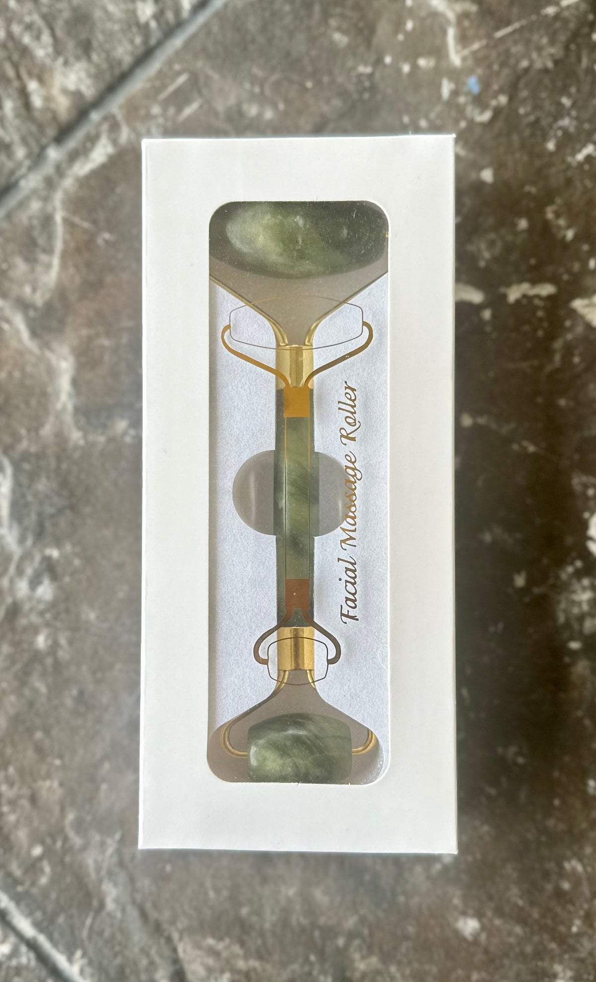 Green double-ended jade facial roller in a white windowed box.