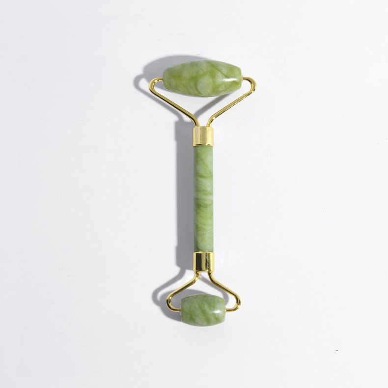 Green double-ended jade roller with smooth heads on a gray surface.
